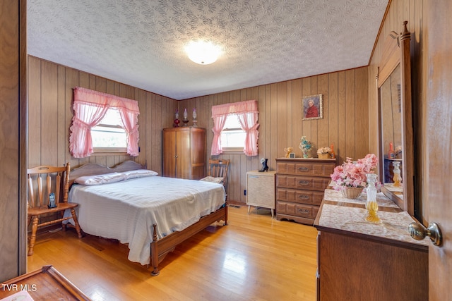 bedroom with wood walls, multiple windows, a textured ceiling, and hardwood / wood-style flooring