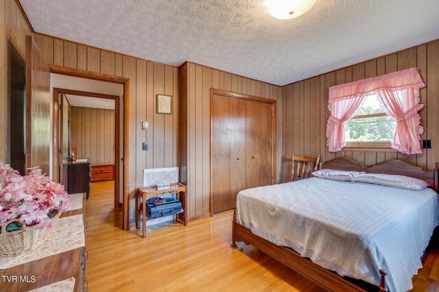 bedroom with wooden walls, a textured ceiling, hardwood / wood-style flooring, and a closet