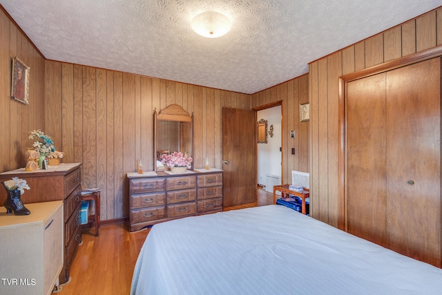 bedroom featuring wooden walls, a textured ceiling, light hardwood / wood-style flooring, and a closet