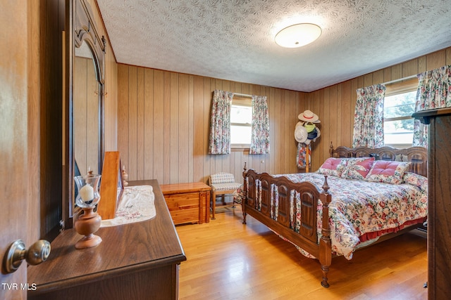 bedroom with wood walls, a textured ceiling, and hardwood / wood-style flooring