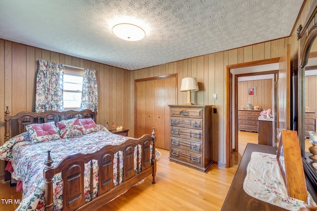 bedroom with a closet, light hardwood / wood-style floors, wooden walls, and a textured ceiling