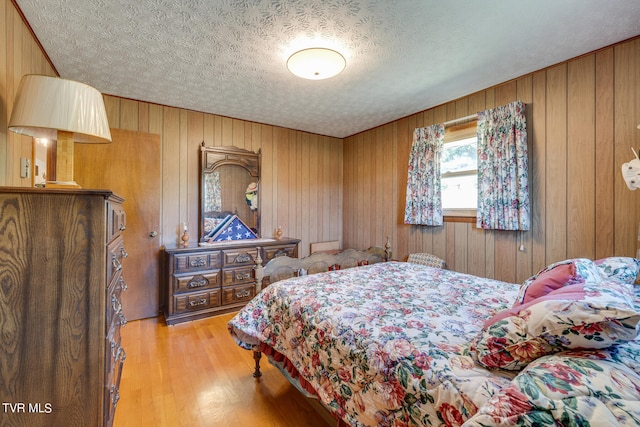 bedroom with light hardwood / wood-style floors, wooden walls, and a textured ceiling