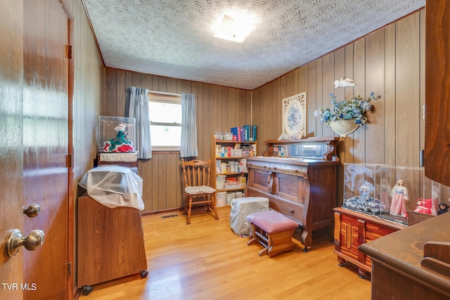 sitting room featuring wooden walls, a textured ceiling, and light wood-type flooring