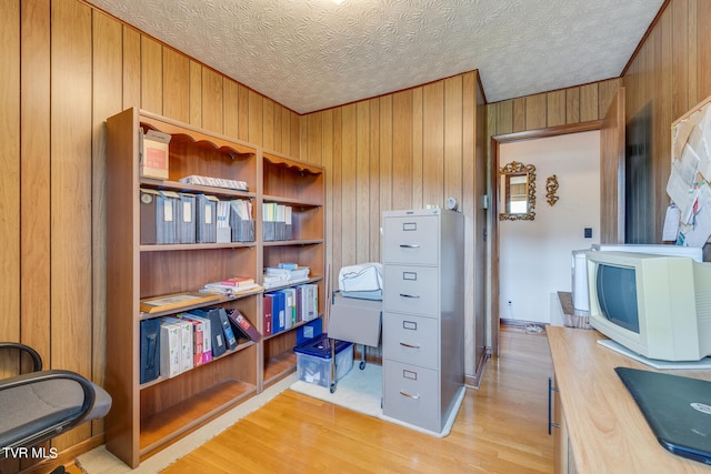 office with wooden walls, light wood-type flooring, and a textured ceiling