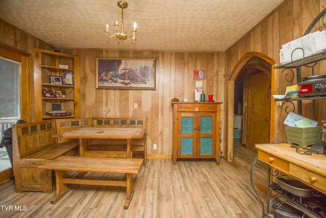 dining room with arched walkways, a notable chandelier, wood walls, and light wood finished floors