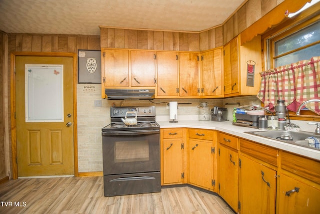 kitchen featuring black electric range, light countertops, light wood-style flooring, a sink, and under cabinet range hood