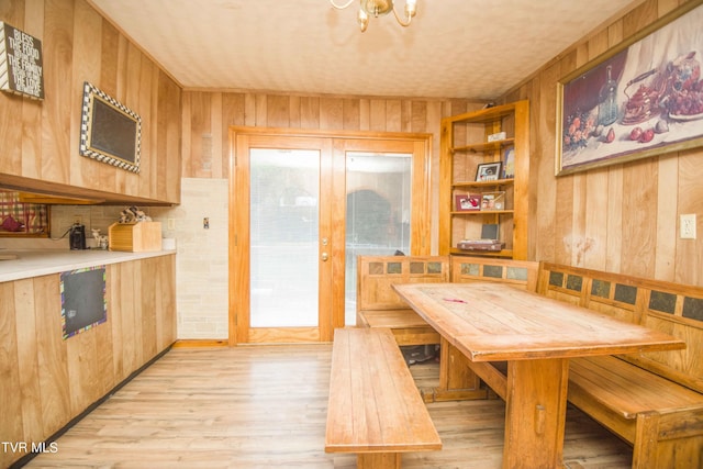 dining space with light wood finished floors, breakfast area, an inviting chandelier, french doors, and wood walls