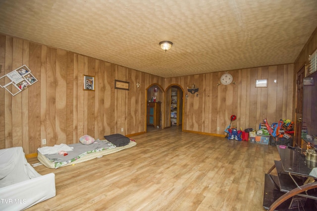 interior space with arched walkways, baseboards, wood finished floors, and wooden walls