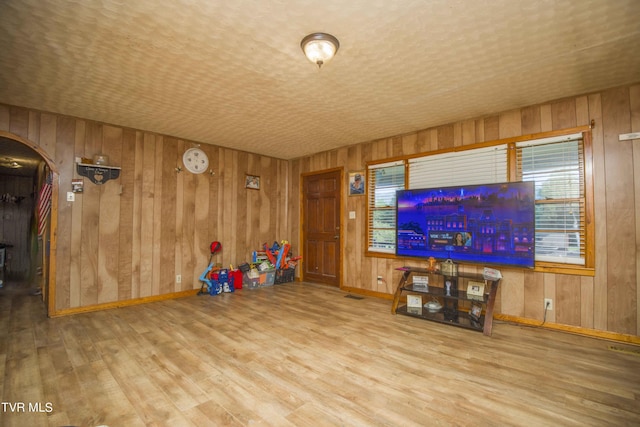 unfurnished living room featuring arched walkways, wood finished floors, and baseboards