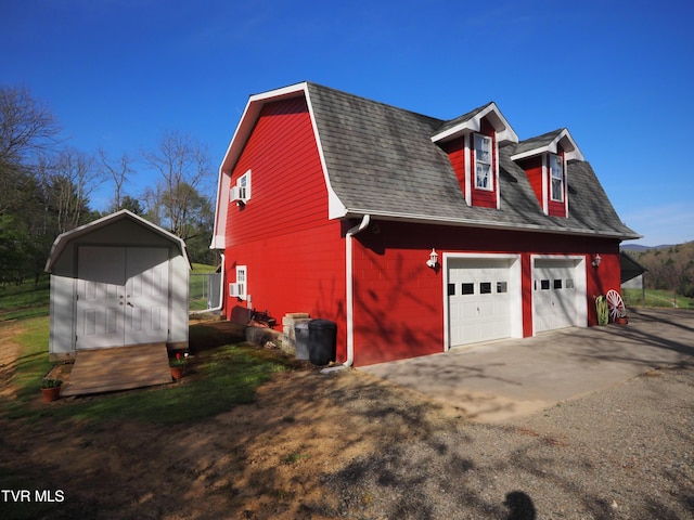 view of side of home featuring an outbuilding, a shingled roof, a detached garage, and a gambrel roof