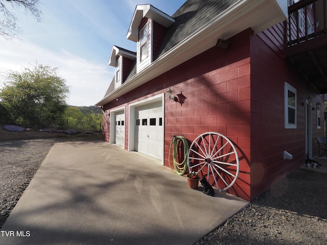 view of side of property with driveway, a shingled roof, and concrete block siding