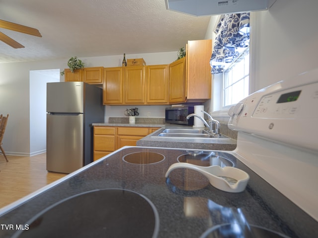 kitchen featuring ceiling fan, stainless steel appliances, a textured ceiling, light wood-type flooring, and a sink