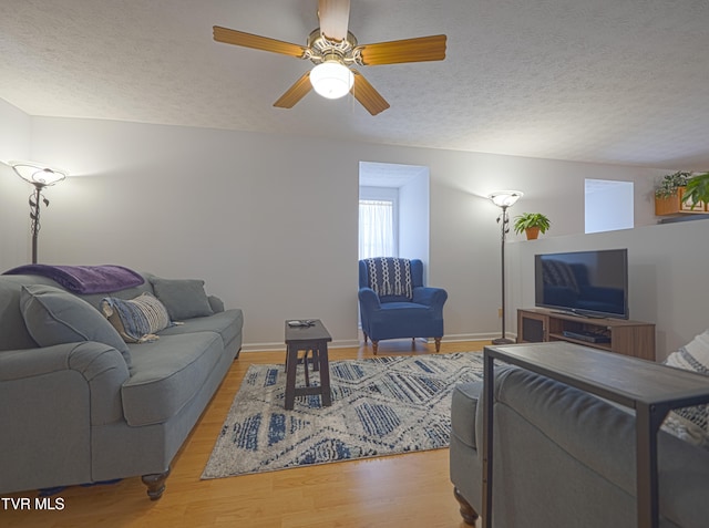 living room with ceiling fan, a textured ceiling, baseboards, and wood finished floors