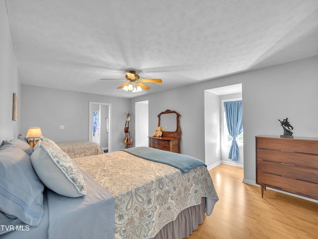 bedroom with light wood finished floors, ceiling fan, baseboards, and a textured ceiling