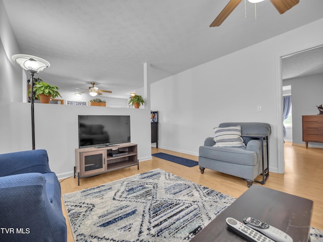 living room with a ceiling fan, baseboards, and wood finished floors