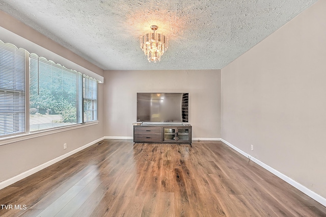 unfurnished living room featuring an inviting chandelier, dark hardwood / wood-style flooring, and a textured ceiling