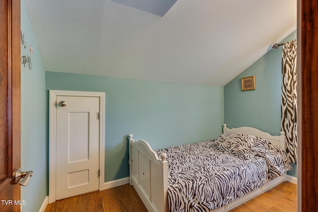 bedroom with vaulted ceiling, baseboards, and wood finished floors