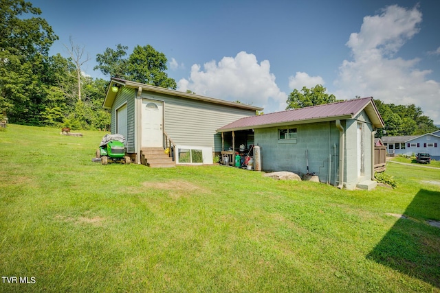 rear view of property with entry steps, concrete block siding, a lawn, and metal roof