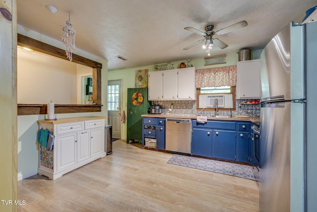 kitchen with a wealth of natural light, blue cabinets, appliances with stainless steel finishes, and white cabinets