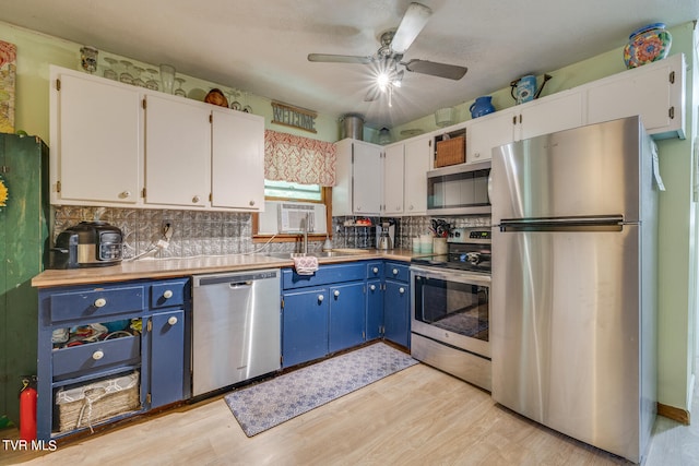 kitchen with appliances with stainless steel finishes, white cabinetry, blue cabinets, and backsplash