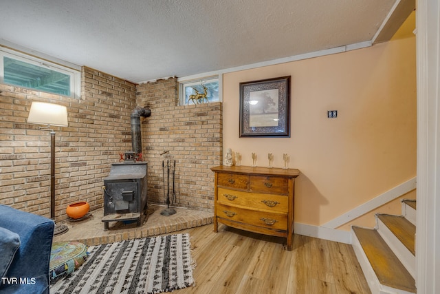 living area with brick wall, light hardwood / wood-style flooring, a textured ceiling, and a wood stove