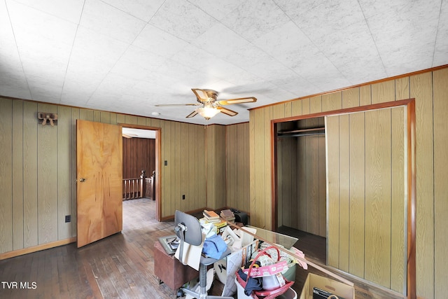 unfurnished bedroom with dark wood-type flooring, wooden walls, ceiling fan, and a closet