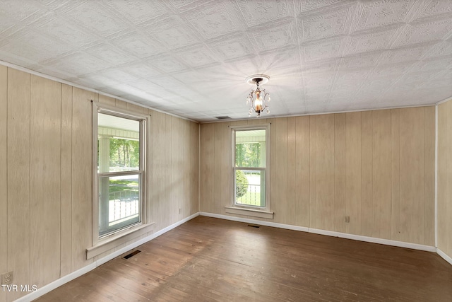 unfurnished room featuring hardwood / wood-style flooring, plenty of natural light, wooden walls, and a chandelier