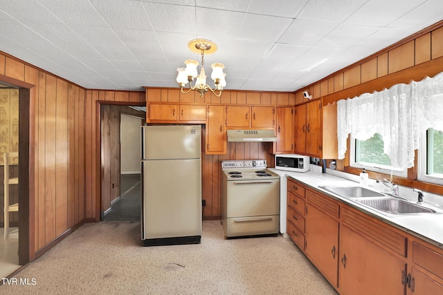 kitchen with pendant lighting, wood walls, sink, white appliances, and an inviting chandelier