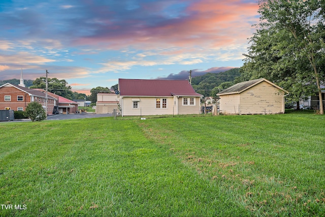 back house at dusk featuring a lawn and an outbuilding