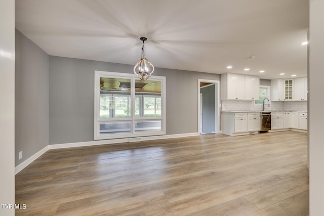 unfurnished living room featuring light hardwood / wood-style flooring, sink, and an inviting chandelier