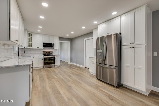 kitchen with appliances with stainless steel finishes, light hardwood / wood-style flooring, sink, and light stone countertops