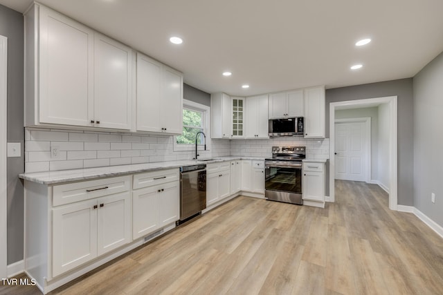 kitchen featuring appliances with stainless steel finishes, white cabinets, light hardwood / wood-style floors, and light stone countertops