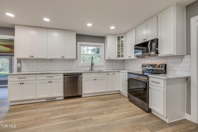 kitchen with decorative backsplash, appliances with stainless steel finishes, a wealth of natural light, and light hardwood / wood-style floors