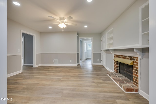 unfurnished living room with ceiling fan, light wood-type flooring, a fireplace, and built in shelves