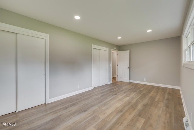 unfurnished bedroom featuring light hardwood / wood-style flooring and two closets