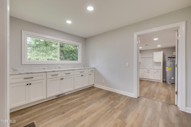 interior space featuring water heater, white cabinets, light wood-type flooring, and light stone counters