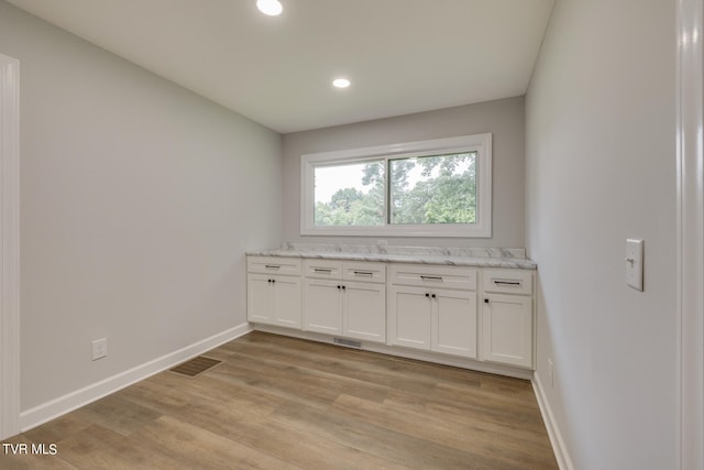 interior space with light wood-type flooring, light stone counters, and white cabinetry