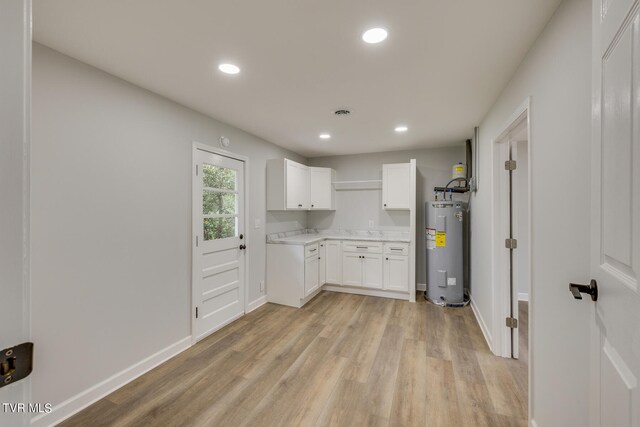 kitchen with electric water heater, light stone countertops, light wood-type flooring, and white cabinetry