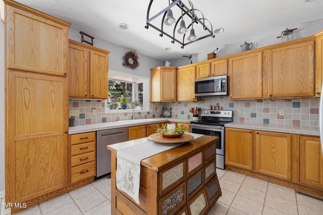 kitchen featuring light tile patterned floors, appliances with stainless steel finishes, a notable chandelier, backsplash, and sink