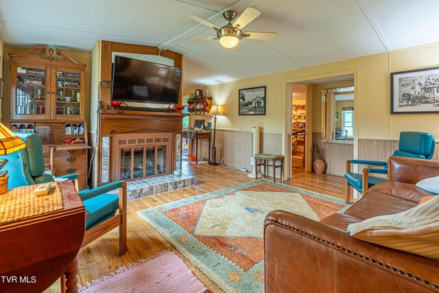 living room featuring a ceiling fan, wood finished floors, a wainscoted wall, lofted ceiling, and a glass covered fireplace