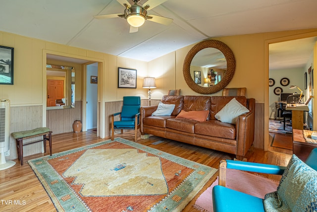 living room with ceiling fan, vaulted ceiling, wood finished floors, and a decorative wall