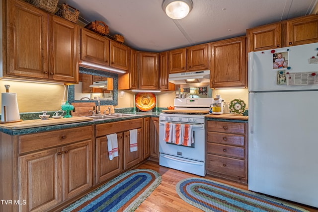 kitchen featuring a sink, light wood finished floors, white appliances, brown cabinetry, and under cabinet range hood