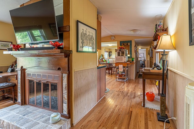 hall featuring wood walls, light wood finished floors, and lofted ceiling