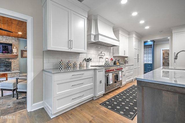 kitchen with white cabinetry, double oven range, sink, and premium range hood