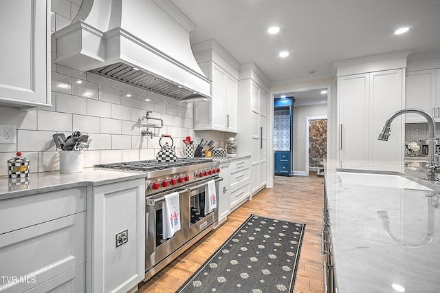 kitchen featuring premium range hood, sink, white cabinets, double oven range, and light wood-type flooring