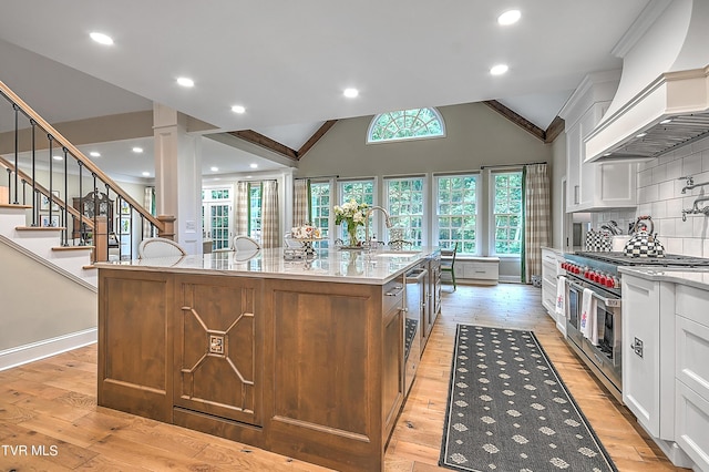 kitchen with sink, double oven range, custom range hood, white cabinets, and a center island with sink