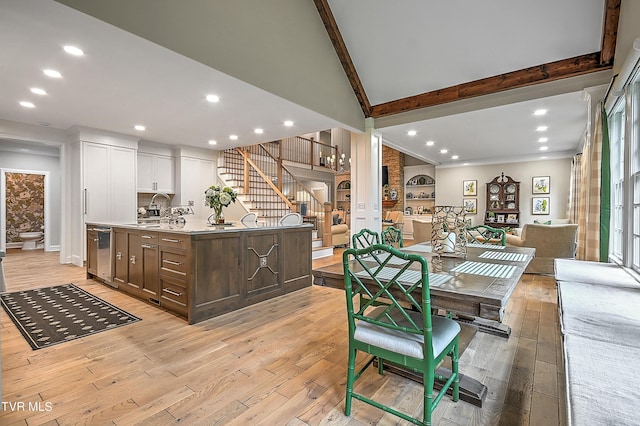 dining area featuring vaulted ceiling with beams, sink, and light hardwood / wood-style flooring