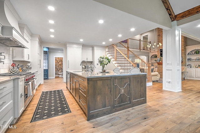 kitchen featuring sink, custom exhaust hood, a kitchen island with sink, range with two ovens, and white cabinets