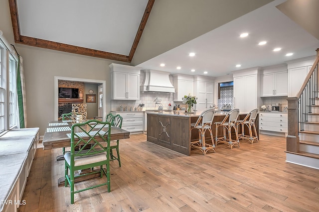 kitchen featuring custom exhaust hood, a kitchen island with sink, white cabinets, and a breakfast bar