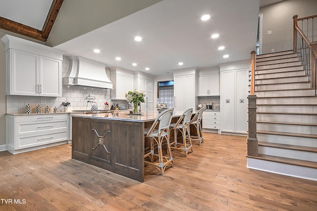 kitchen featuring custom exhaust hood, a kitchen breakfast bar, white cabinets, and a center island with sink